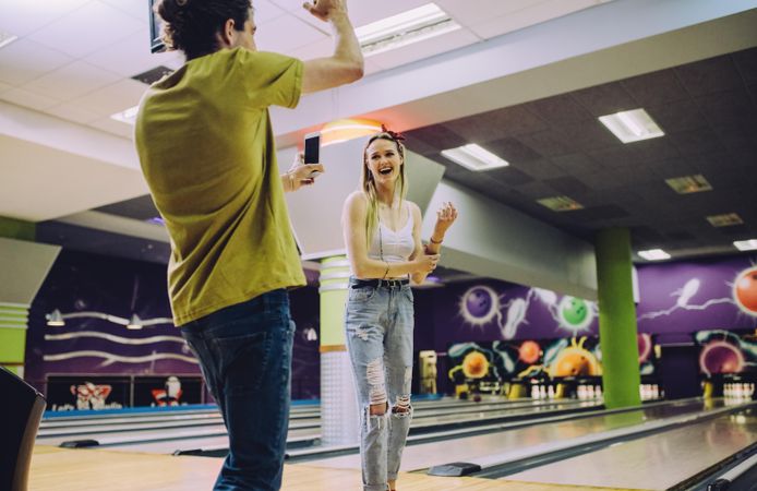 Young man recording woman playing bowling at club