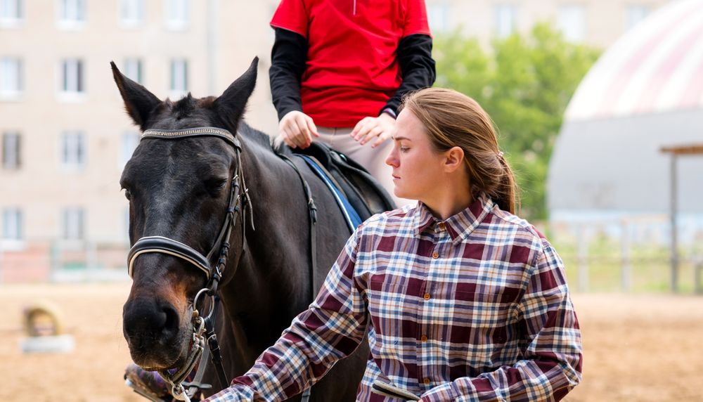 Instructor leads horse while rider focuses during riding lesson.