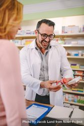 Professional male pharmacist showing medicine to female customer in pharmacy 0VWBO5