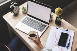 Person holding a cup of coffee while sitting at a desk with laptop in office