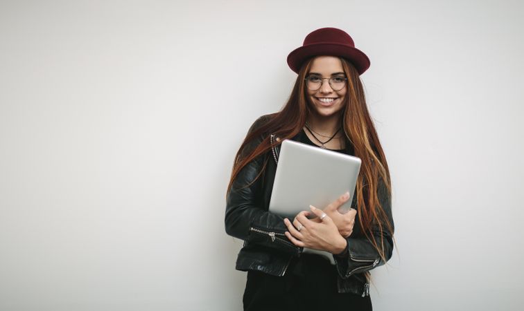 Cheerful businesswoman wearing hat and eyeglasses holding laptop