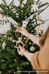 Cropped image of woman putting an ornament on Christmas tree bGXla0
