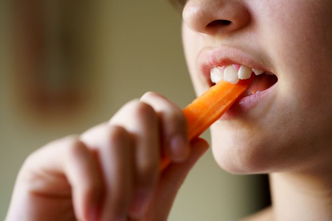 Anonymous teenage girl biting into carrot stick