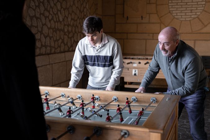 A father and his son are playing table football game and having fun together