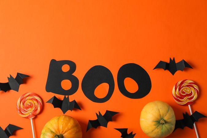 Word Boo, candy, decorative bats and pumpkins on orange background, copy space