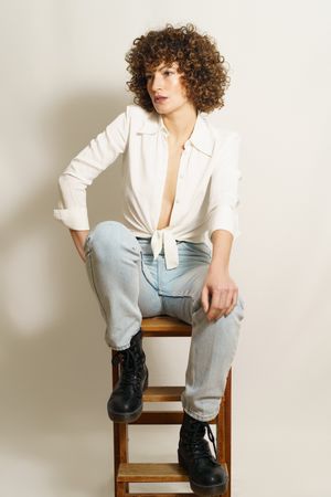 Woman in jeans and boots sitting on wooden stool in studio shot