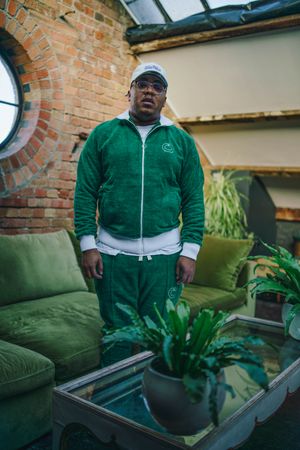 Stylish Black man in green fuzzy track suit standing in industrial loft living room