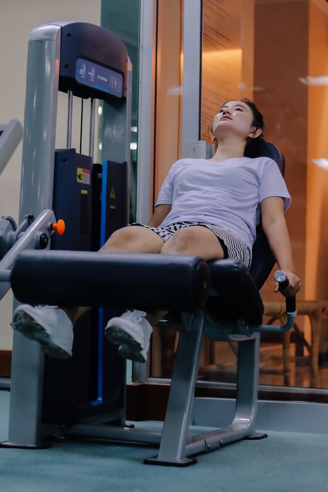 woman using leg extension machine at gym. sitting with legs positioned under padded machine bar.