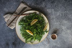 Top view of healthy vegetable salad with organic arugula, lemon and flax seeds on stone background