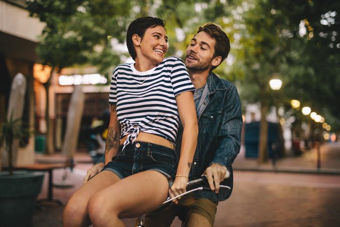 Smiling woman sitting on bicycle handlebar with her boyfriend