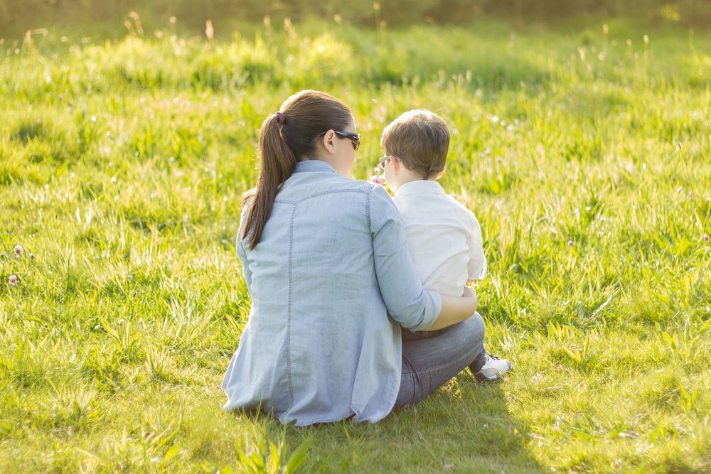 Cute son giving a bouquet of flowers to his mother sitting in a field