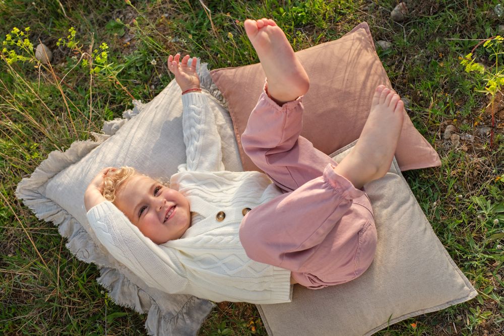 Cute girl lying on cozy pillow on glade in countryside
