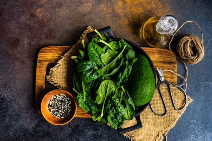 Top view of fresh spinach on board with bowl of seasonings