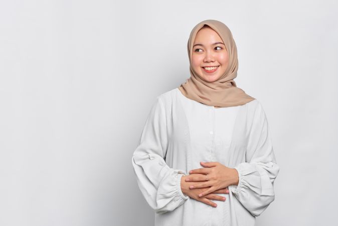 Smiling Muslim woman in headscarf in light blouse with hands resting on her torso