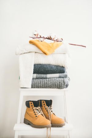 Pile of folded sweaters on light background with yellow boots, dried cotton, vertical composition