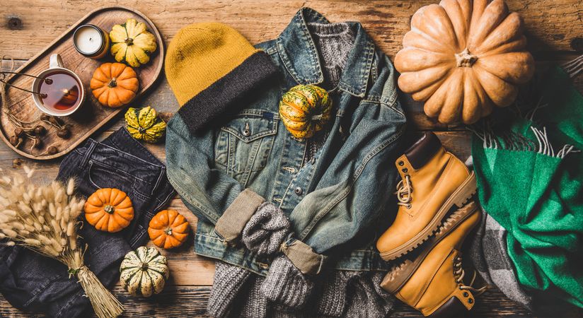 Flat-lay of denim jacket, sweater, jeans, scarf, hat, yellow boots, pumpkins, candle, tea