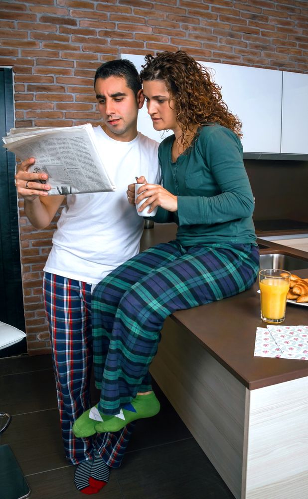 Curious couple in pajamas reading paper together in kitchen at breakfast time
