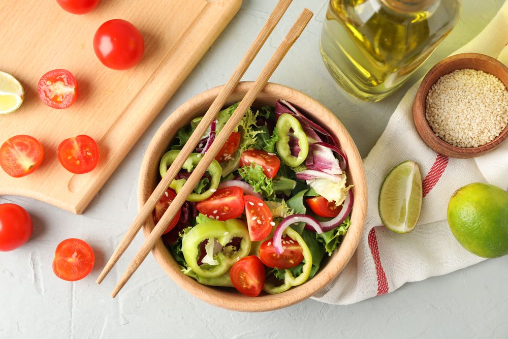 Salad with sesame and kitchen accessories on grey background, top view