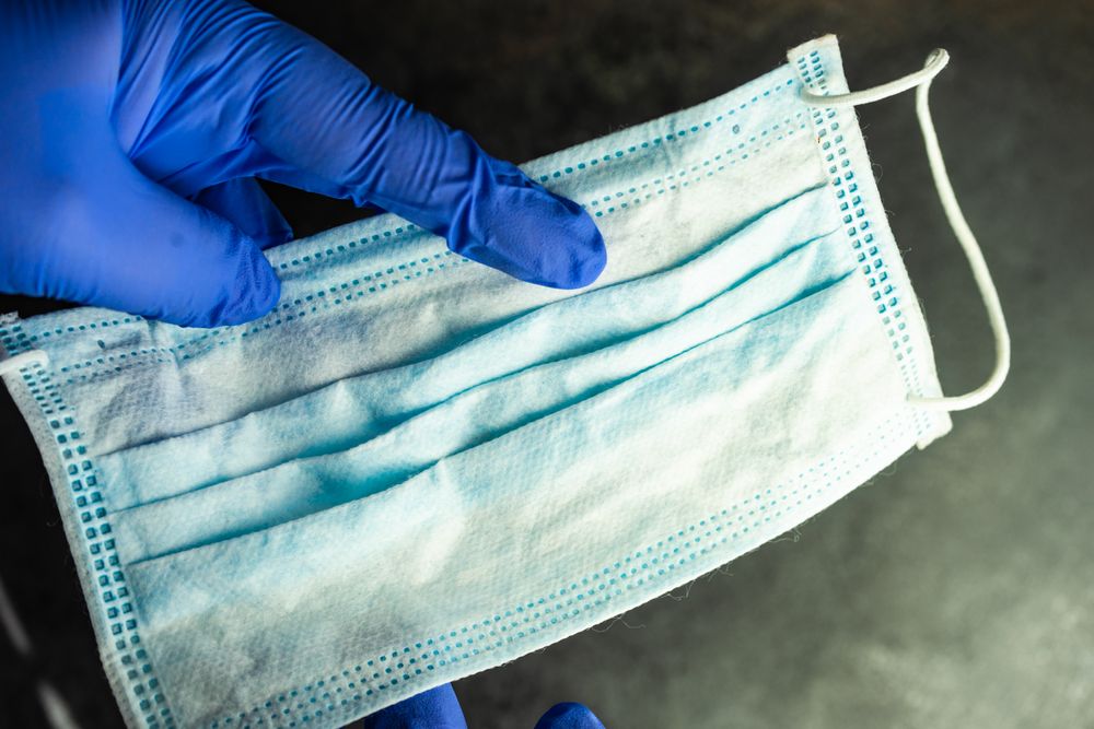Hands wearing blue latex gloves with blue facemask