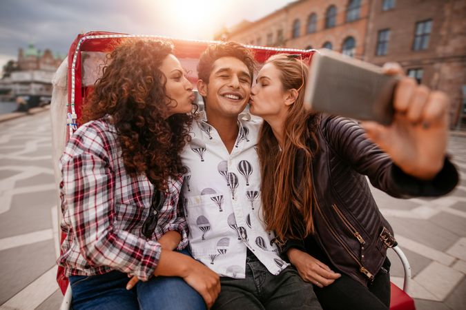 Women kissing man and taking selfie on tricycle
