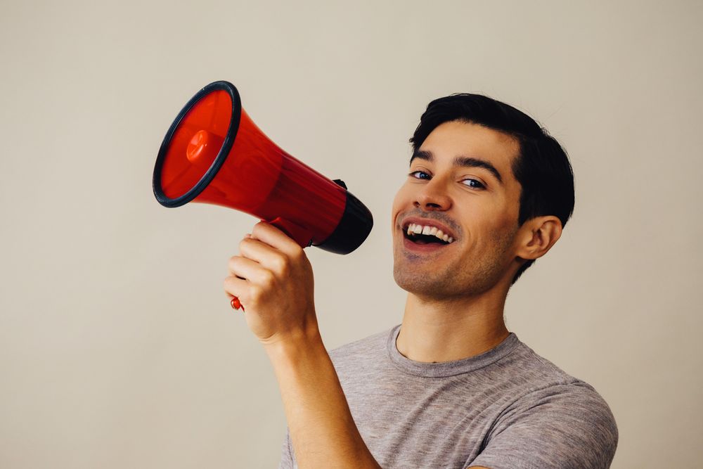 Side view of Hispanic male speaking through red loudspeaker