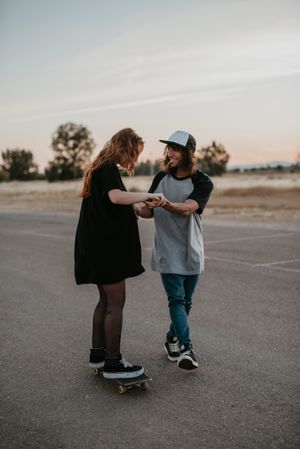 Man helping girlfriend to skate on road