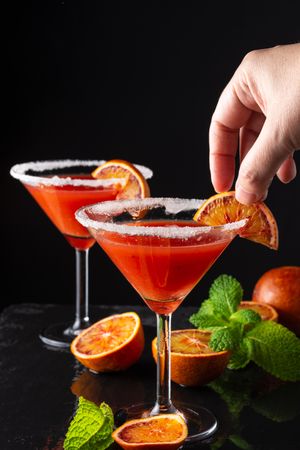 Person adding orange garnish to salt rimmed cocktail
