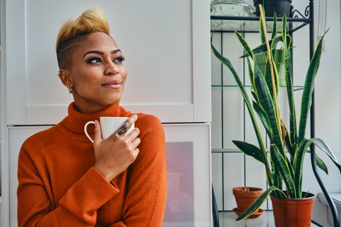 Black woman thinking deeply over a cup of coffee in a bright home