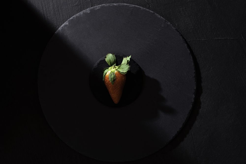 Single strawberry on dark platter in harsh ligh