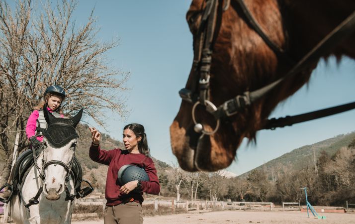 Young woman teaching girl to ride horse