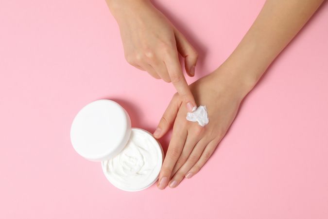 A jar of hand cream on a light pink background.