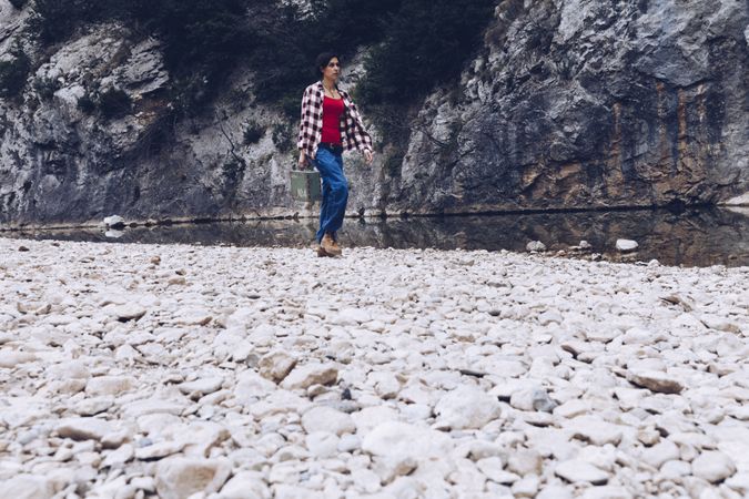 Woman with case walking on shore above stream