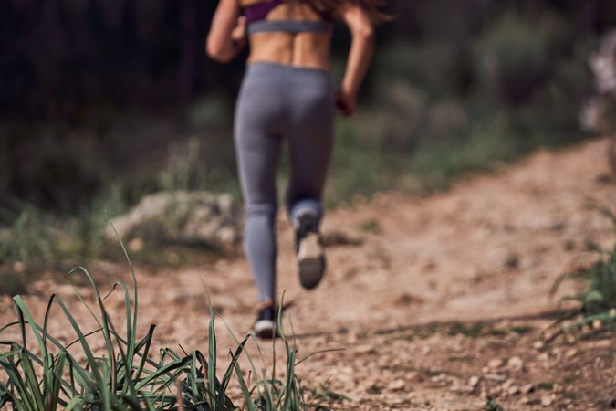 Crop faceless female jogger running on pathway in woods