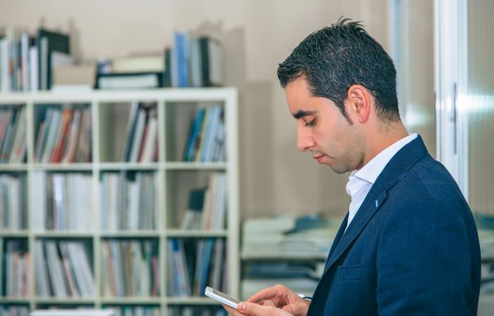 Side view of businessman looking down at smartphone in office