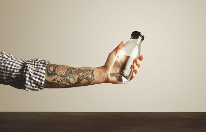 Tattooed arm holding glass water bottle