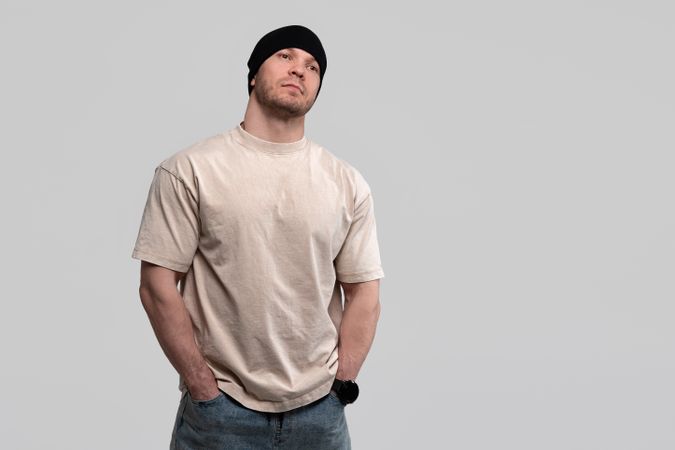 Man in beige t-shirt and beanie, hands in pockets