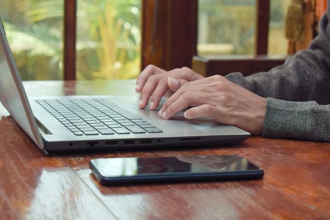 Close up side view of young man typing on laptop on wooden table