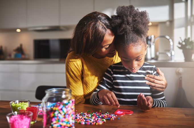 Black mother hugs daughter as she creates arts and crafts at home