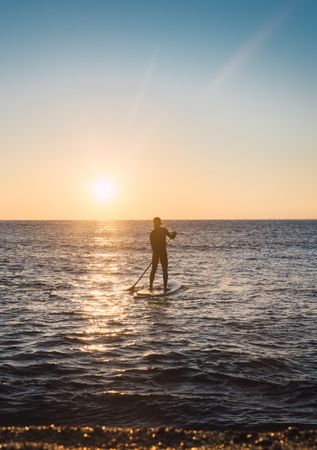Man practicing paddle surfing with neoprene in a sunrise