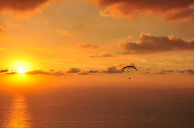Silhouette of parachute flying over the sea during sunset