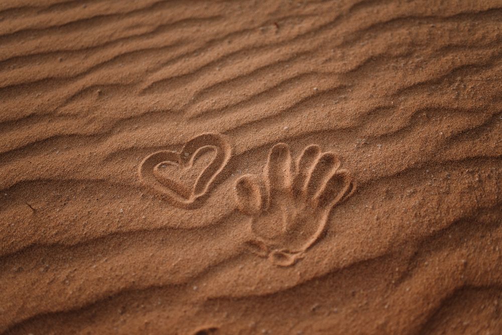 Heart drawn in sand and trace of palm on beach