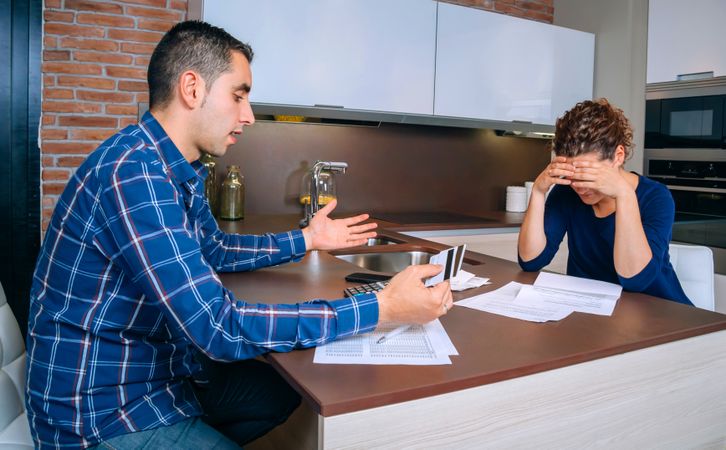 Woman with head down as her and her partner have tense discussion over bills