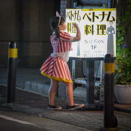 Back view of girl in striped dress standing on sidewalk at night in Itoshima, Fukuoka, Japan
