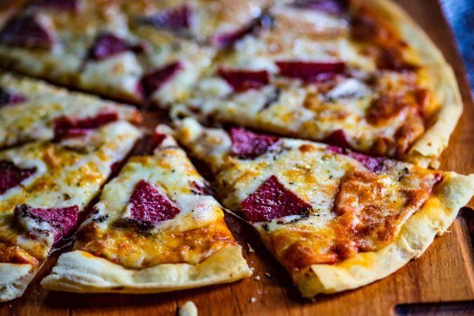 Close up of cheese pizza with slices of meat on wooden board