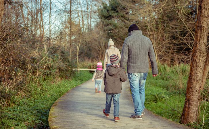 Back of parents walking with their young children along trail in forest