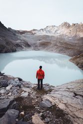Man in red jacket standing on waterside of frozen lake during daytime