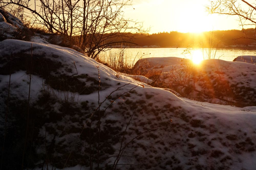 Rocky peaceful shore with snow crust in sunrays