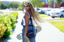 Smiling female in denim overalls standing with skateboard and looking behind her