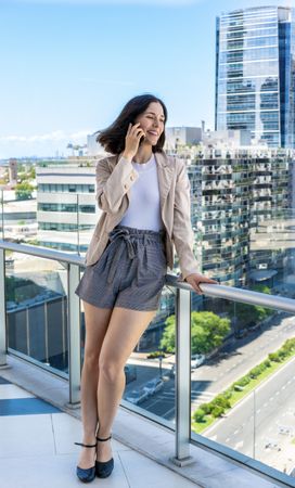 A woman is taking a break from work and chatting on her cell phone while standing on a balcony