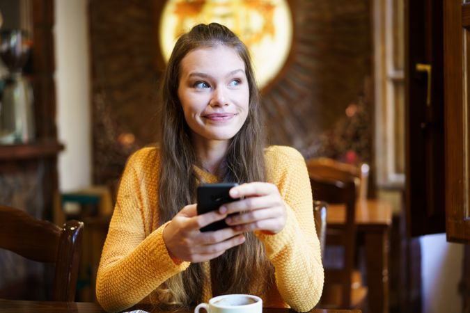 Smiling Young Woman Using Smartphone in Cozy Cafe Setting